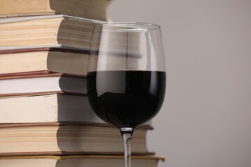 Red wine in glass and stack of books on light grey background, closeup. Space for text