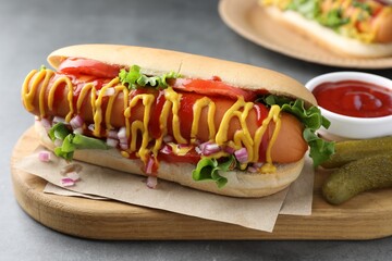 Delicious hot dog with sauces, lettuce, onion and pickles on grey textured table, closeup