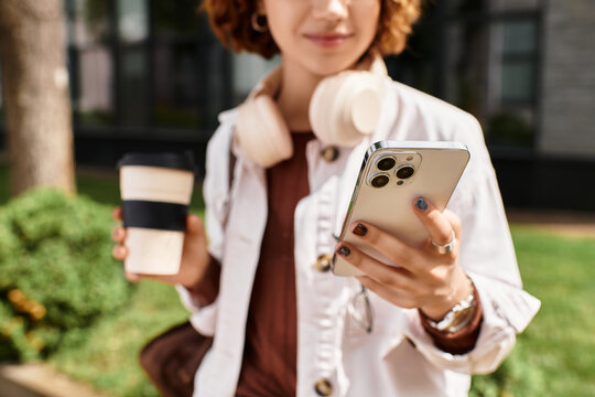 Young woman enjoying coffee while using her smartphone near modern office building