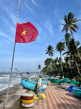 tropical beach and fisherman village with flag on coast of Vietnam with palm trees and round colored boats