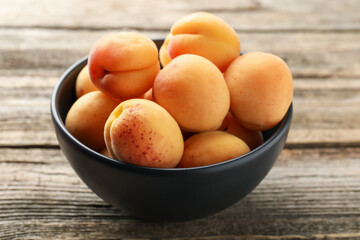 Fresh apricots in bowl on wooden table, closeup