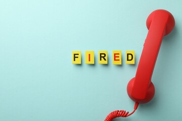 Dismissal. Word fired and telephone handle on light blue background, flat lay