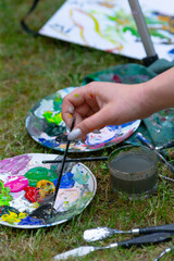 Obraz premium A person is artistically painting with a brush on a colorful palette while seated on the soft grass outdoors, enjoying the process