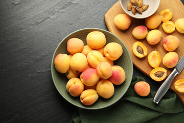 Fresh ripe apricots in bowl, kernels and knife on black table, flat lay. Space for text