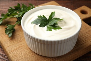 Tasty sour cream with parsley on wooden table, closeup