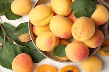 Fresh ripe apricots in bowl and green leaves on white table, flat lay