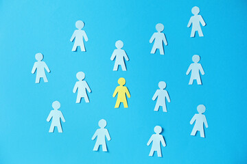 Paper human figures and yellow one on light blue background, flat lay