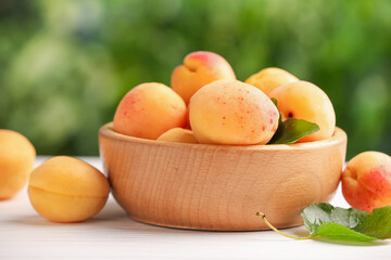 Fresh ripe apricots in bowl on white wooden table outdoors, closeup