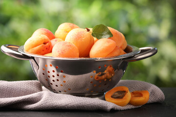 Fresh ripe apricots in colander on black table outdoors, closeup
