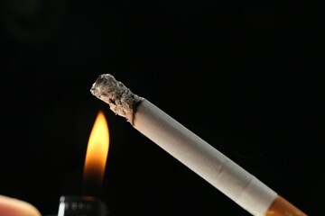 Lighting up cigarette on black background, closeup