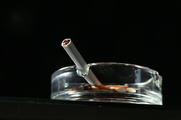 Cigarette butts in ashtray on black background, closeup