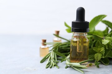 Bottle of essential oil and herbs on light grey table, closeup. Space for text