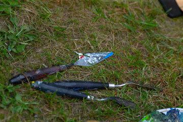 A collection of colorful palette knives is scattered across the grass, waiting to be picked up or...