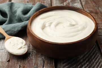 Delicious sour cream in bowl and spoon on wooden table, closeup