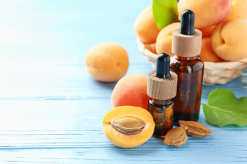 Bottles of essential oil, fresh apricots and kernels on light blue wooden table, closeup. Space for text