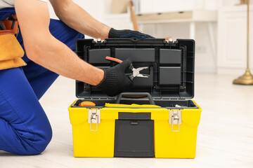 Professional repairman with tool box and pliers indoors, closeup
