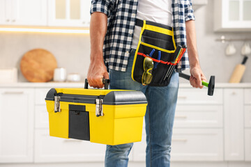 Professional repairman with tool box and hammer indoors, closeup