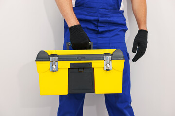 Professional repairman with tool box on light grey background, closeup