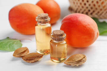 Bottles of essential oil, fresh apricots and kernels on white wooden table, closeup