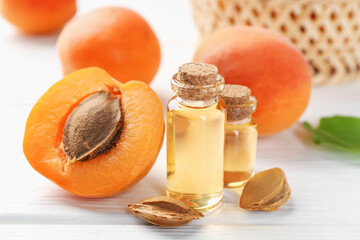 Bottles of essential oil, fresh apricots and kernels on white wooden table, closeup