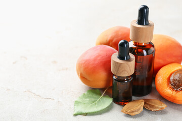 Bottles of essential oil, fresh apricots, kernels and green leaf on light grey table, closeup....