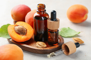Bottles of essential oil, fresh apricots, kernels and green leaves on light grey table, closeup