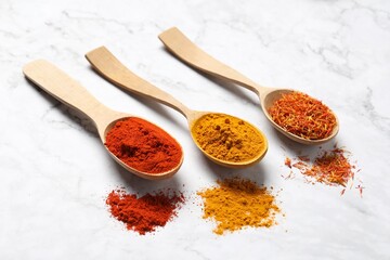 Different aromatic spices in wooden spoons on white marble table, closeup