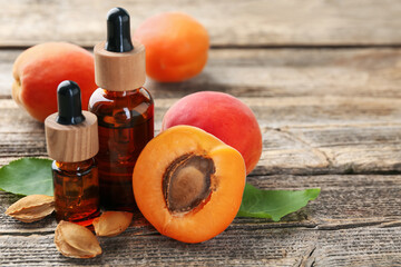 Bottles of essential oil, fresh apricots, kernels and green leaves on wooden table, closeup. Space...