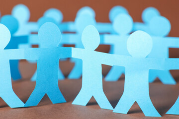 Paper figures of people holding hands on brown background, closeup
