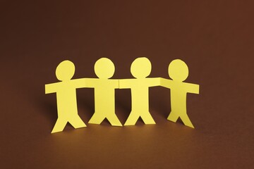 Paper figures of people holding hands on brown background, closeup