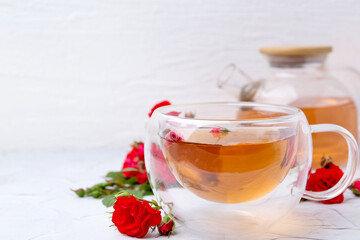 Aromatic tea in glass cup, roses and green leaves on white table, closeup. Space for text