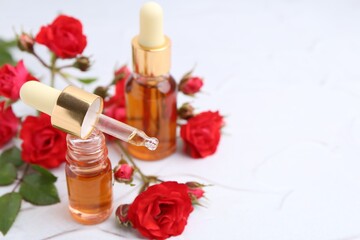 Bottles of essential oil and red roses on white table, closeup. Space for text