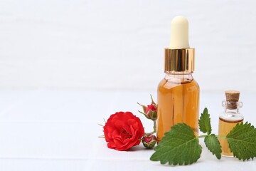 Bottles of essential oil and red roses on white table, closeup. Space for text