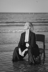 Girl in a black business suit in the sea on the beach on a wooden retro chair. Photo model....