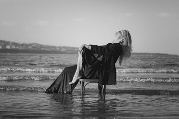 Girl in a black business suit in the sea on the beach on a wooden retro chair. Photo model....