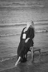 Girl in a black business suit in the sea on the beach on a wooden retro chair. Photo model....