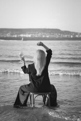 Girl in a black business suit in the sea on the beach on a wooden retro chair. Photo model....