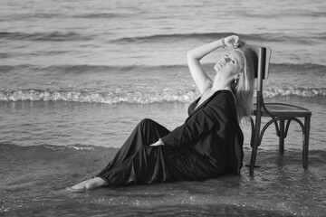 Girl in a black business suit in the sea on the beach on a wooden retro chair. Photo model....