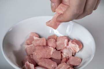 Human hand places fresh raw diced meat into white bowl, preparing healthy ingredients for home cooking or a nutritious meal