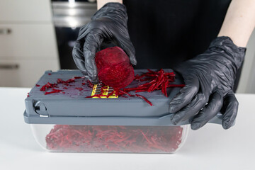 Hands in black gloves expertly grate a vibrant red beetroot using a kitchen shredder for efficient...