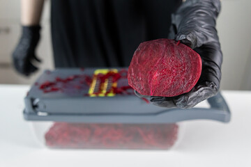 Person in black gloves holds a vibrant, freshly cut beetroot half above a vegetable slicer,...