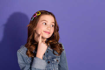Charming young girl in denim jacket with heart accessories posing thoughtfully against violet background