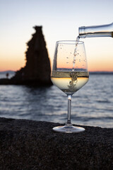 A person pours a glass of Albariño wine with the tower of San Sadurniño in the background. Silhouette at sunset.