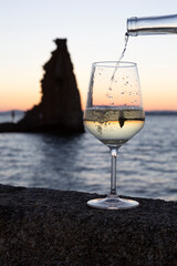 A person pours a glass of Albariño wine with the tower of San Sadurniño in the background. Silhouette at sunset.
