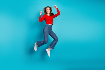 Cheerful young woman in casual outfit jumping joyfully against vibrant blue background showcasing fun and energy