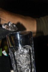 A bartender pours clear ice cubes into a large clear glass	
