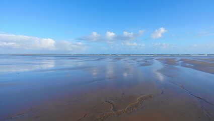 Reflective beach sand under a bright blue sky with wispy clouds