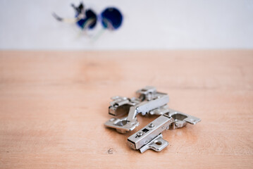 Close-up view of new furniture hinges placed on wooden table, with blurred electrical wiring in the...