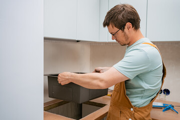 Professional plumber carefully placing new sink into countertop cutout during kitchen renovation,...