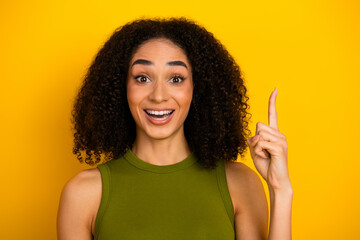Cheerful young woman pointing with enthusiasm while wearing a green top against a bright yellow...